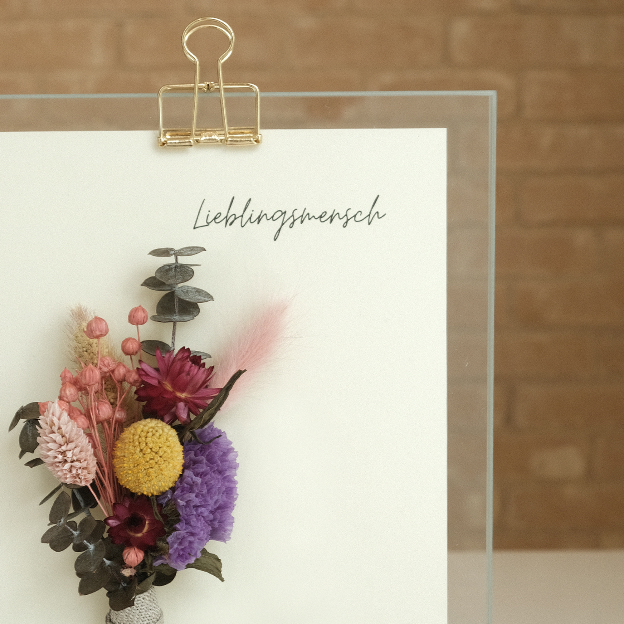 Detailansicht von einem Glasaufsteller mit der Aufschrift "Lieblingsmensch" und floraler Dekoration mit Trockenblumen.
