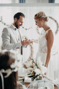 Brautpaar bei der Ringübergabe. Die Braut hält in ihrer linken Hand einen Brautstrauß aus Trockenblumen.