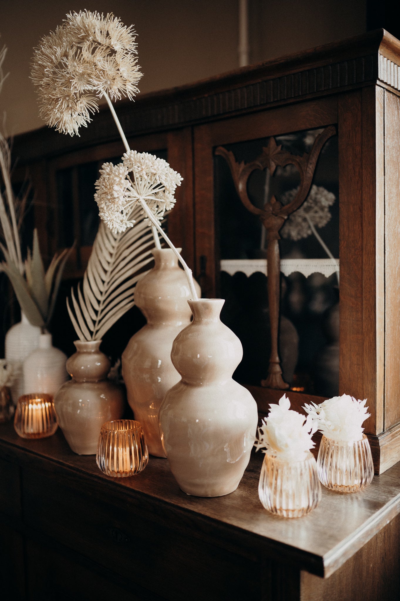 Vasen mit Kunst- und Trockenblumen, drapiert auf einem Holzmöbel.